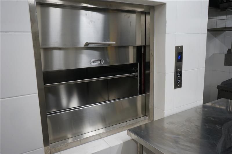 Stainless steel dumbwaiter in a kitchen, with call buttons.
