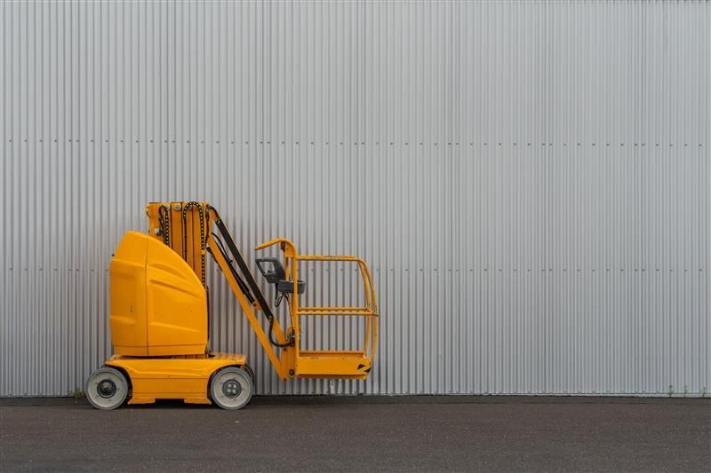 Yellow aerial lift platform parked against a gray, corrugated metal wall.