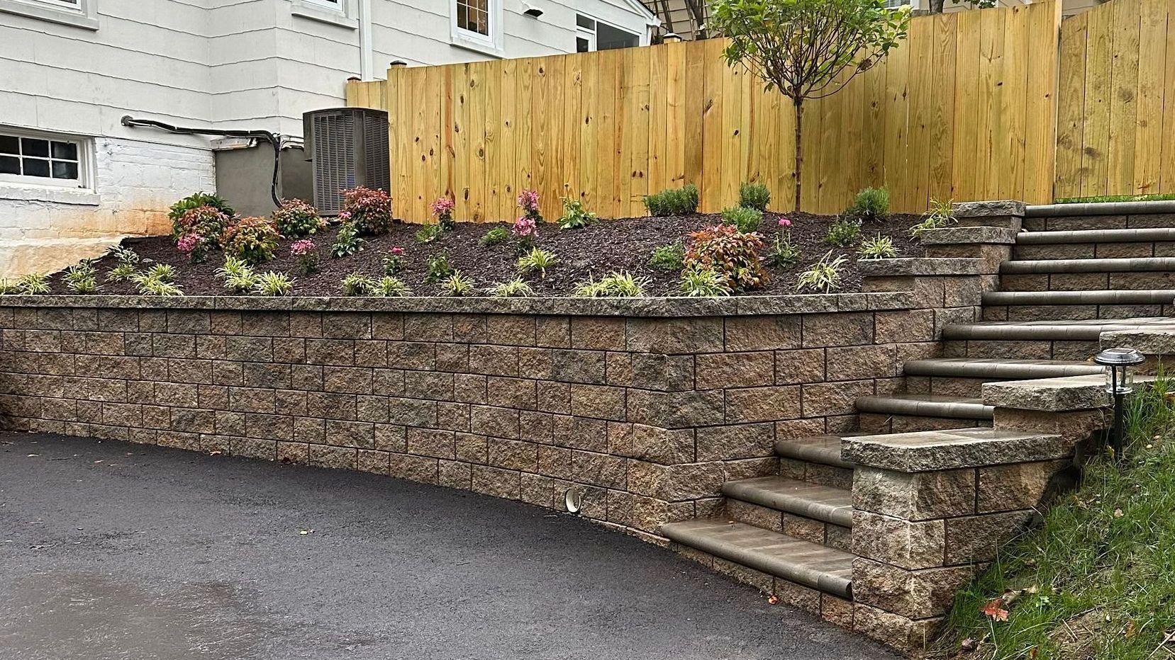 A stone wall with stairs leading up to it next to a wooden fence.