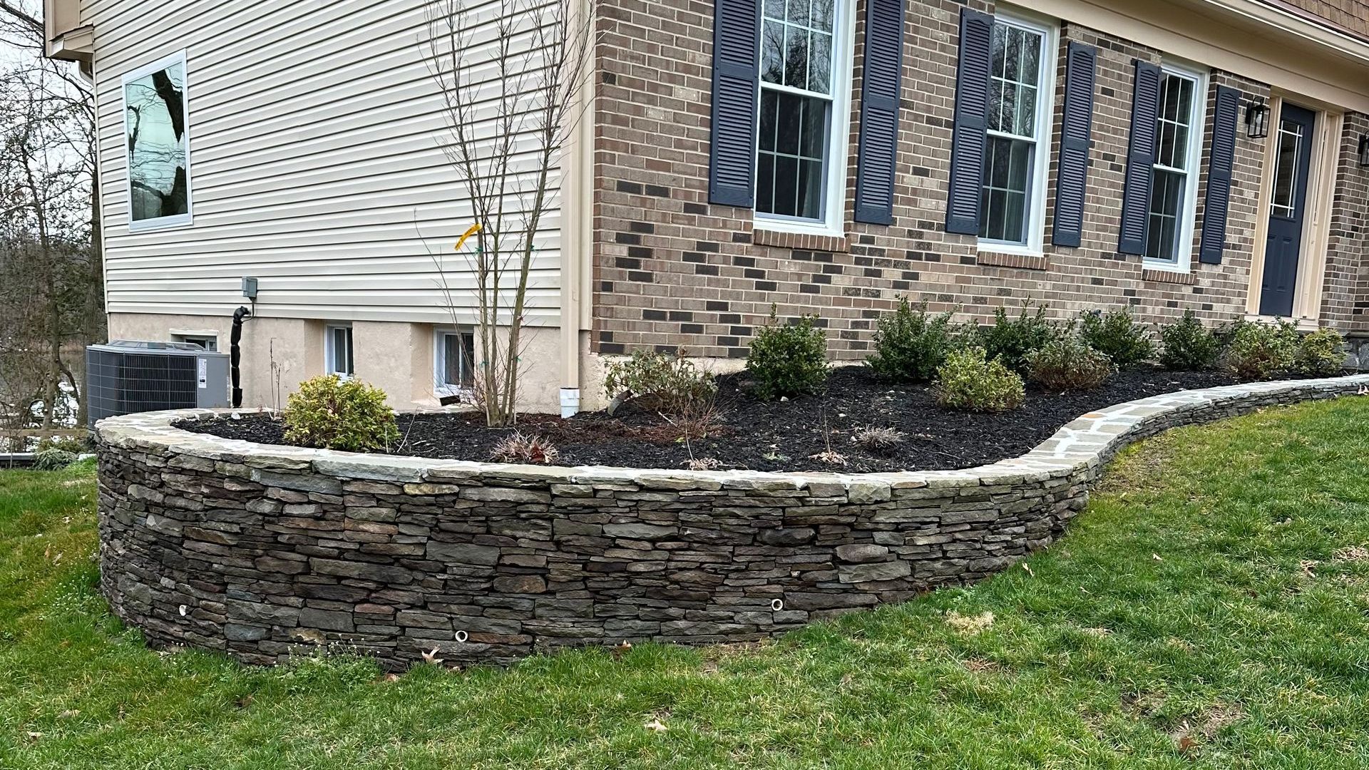 A large brick house with a stone wall in front of it.