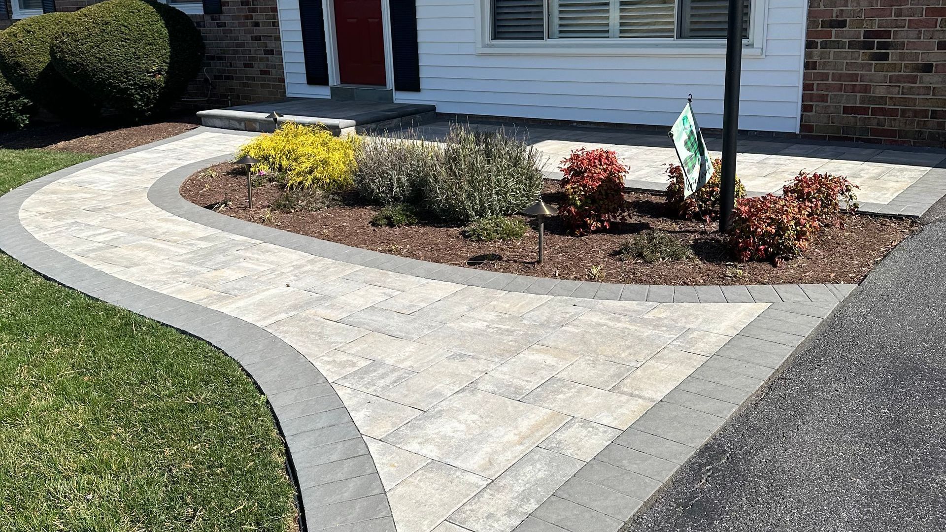 A brick walkway is leading to a house with a red door.