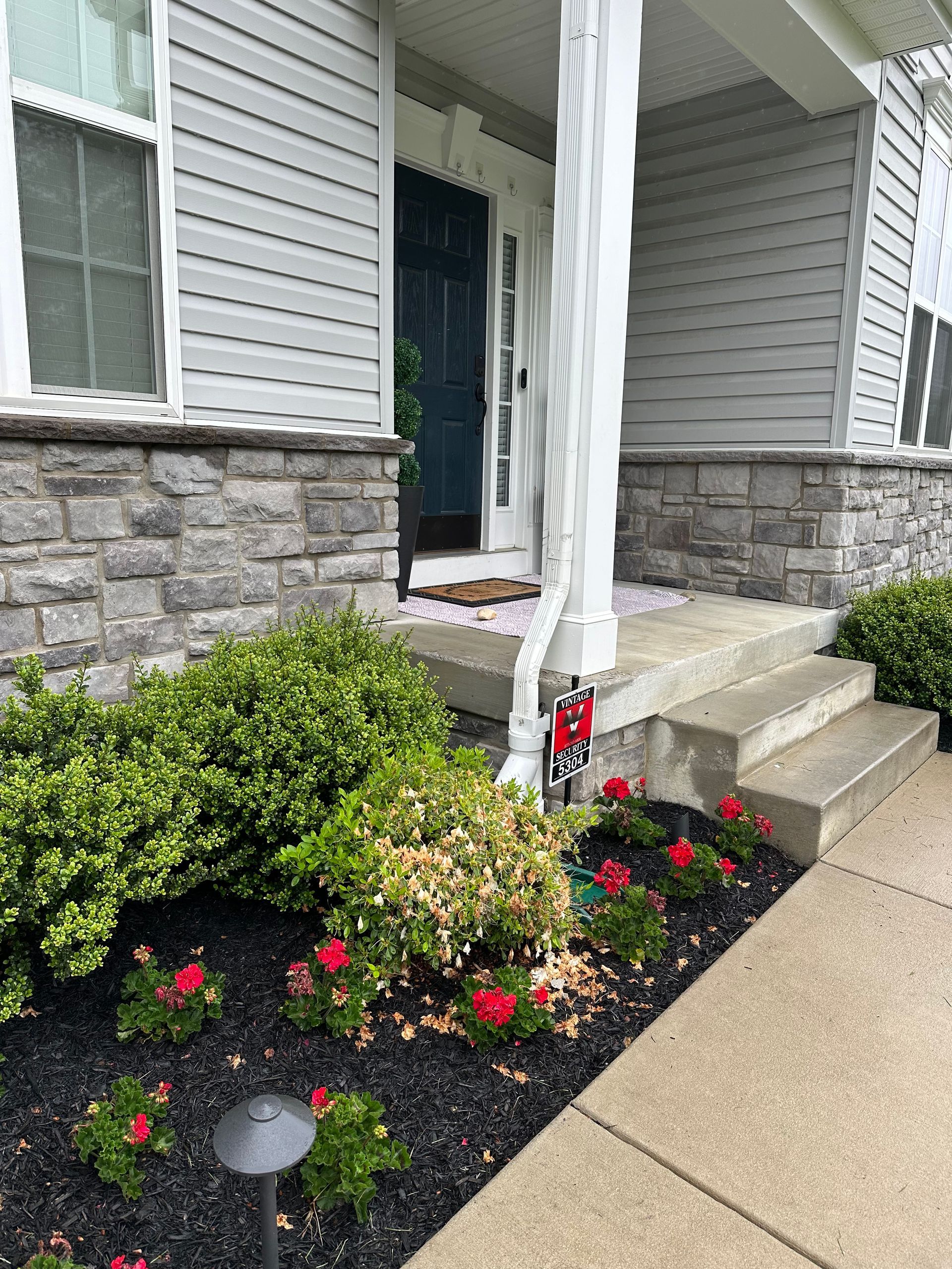 The front of a house with a porch and flowers in front of it.