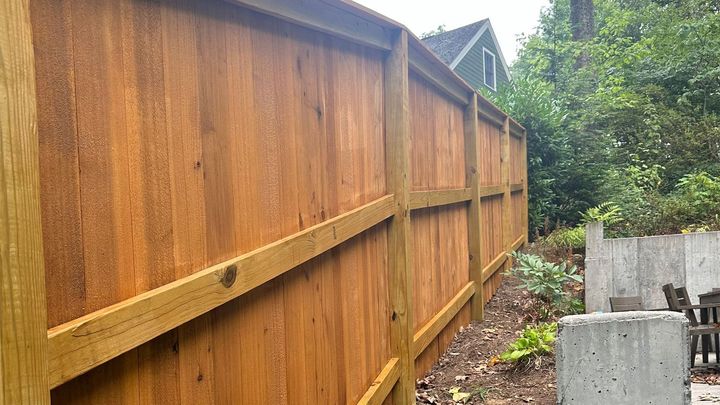 A wooden fence is sitting next to a concrete wall in a backyard.