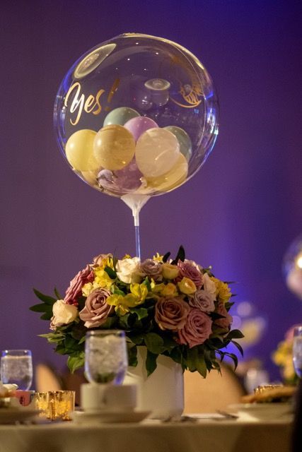 A table with a vase of flowers and balloons on it.