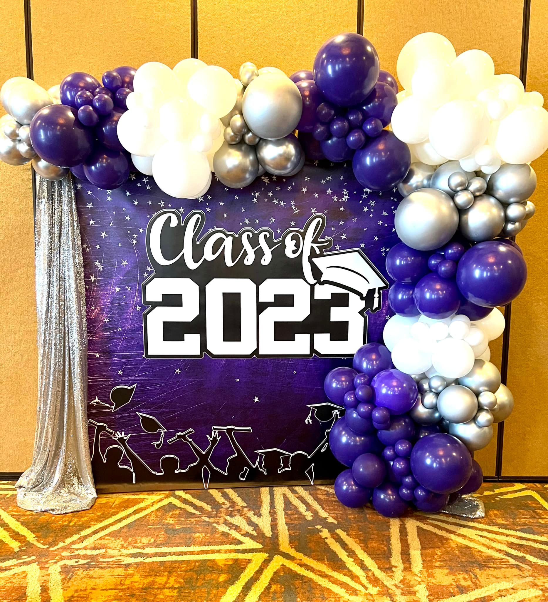 A purple and silver balloon arch with a sign that says class of 2023.