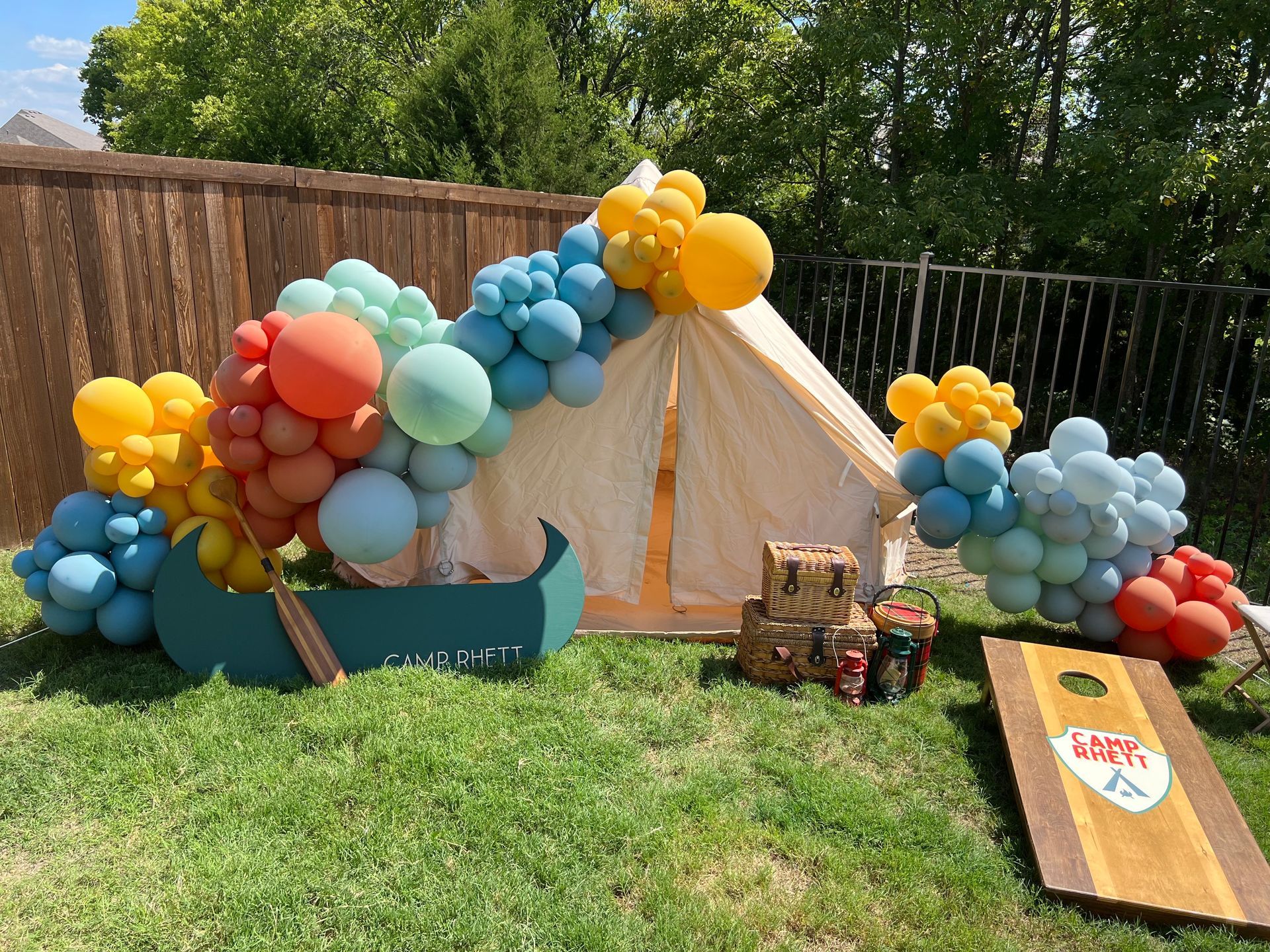 A tent is decorated with balloons and a cornhole board.