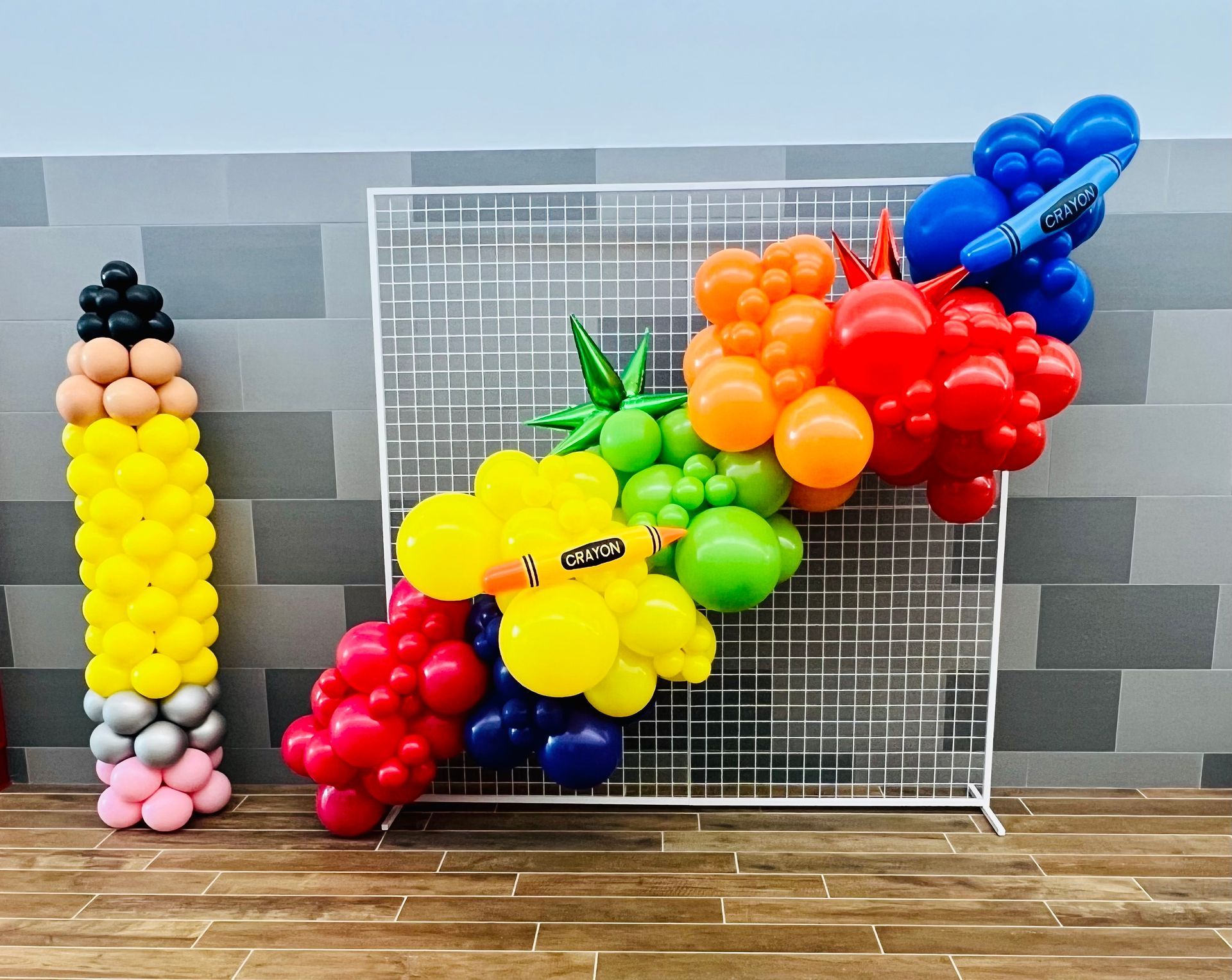 A pencil made out of balloons is sitting next to a wall.