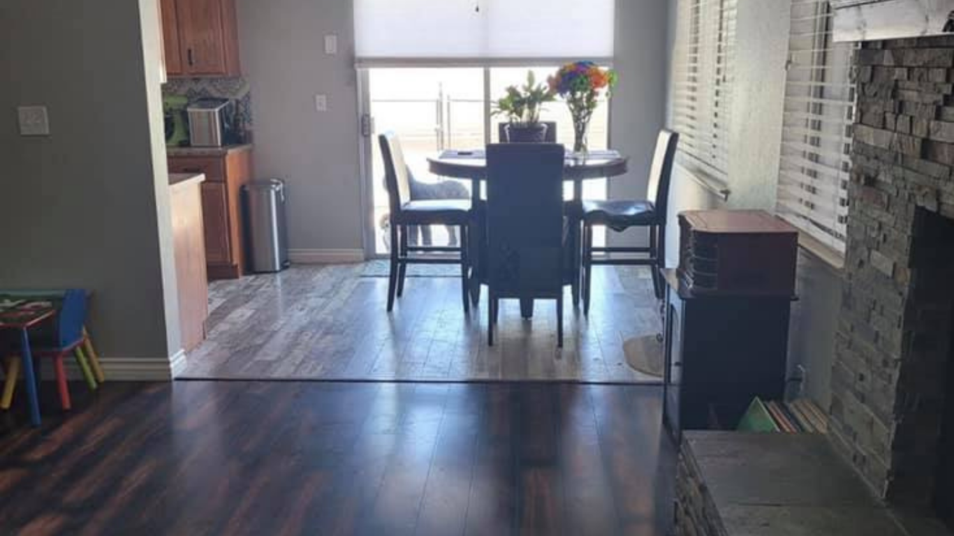 An interior view of a dining area with a table and four chairs, situated between a kitchen and a stone fireplace.