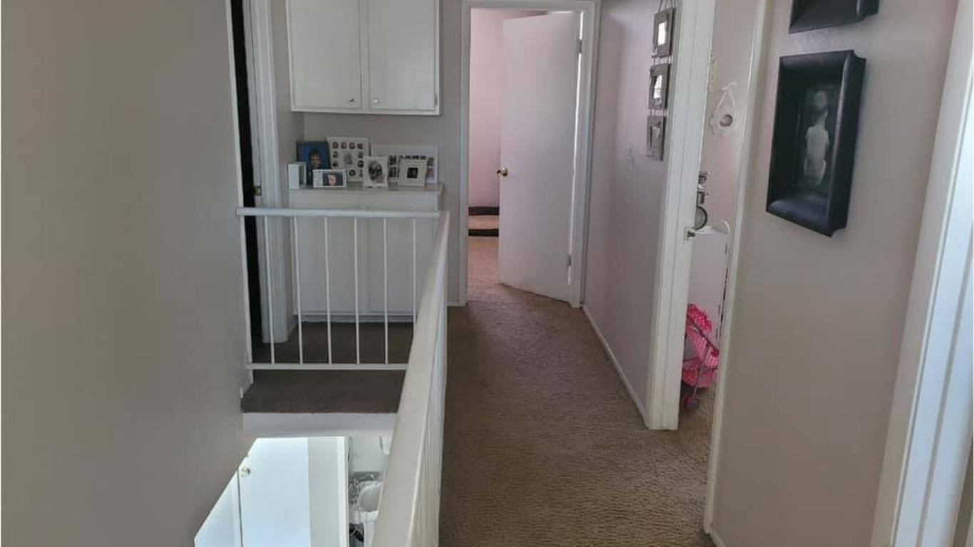 A view from a carpeted hallway landing showing a stairwell railing, a white cabinet, and doorways to other rooms.