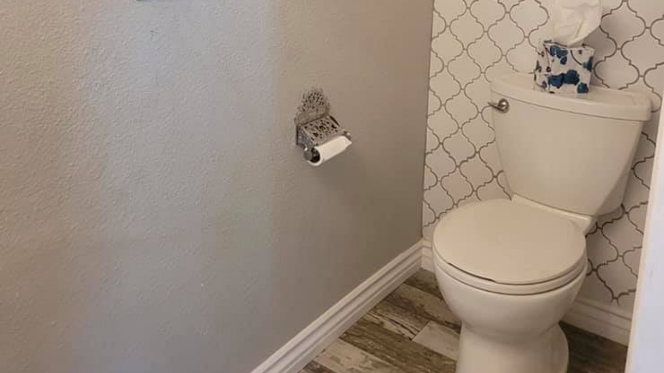 A toilet with an empty roll holder on a grey wall, next to a wall with white and black geometric pattern wallpaper.