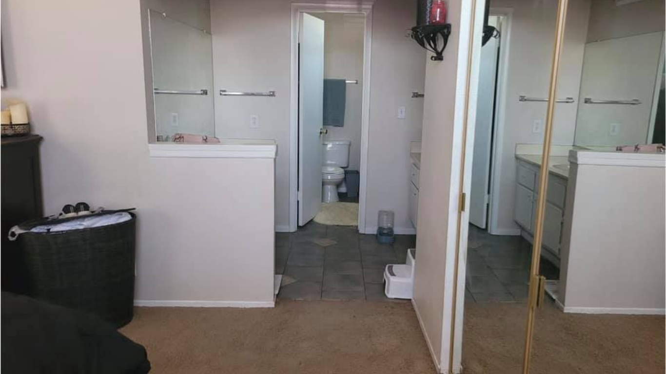 A view from a bedroom into an open bathroom with carpeted flooring, a tile-floor toilet area, and a large mirror.