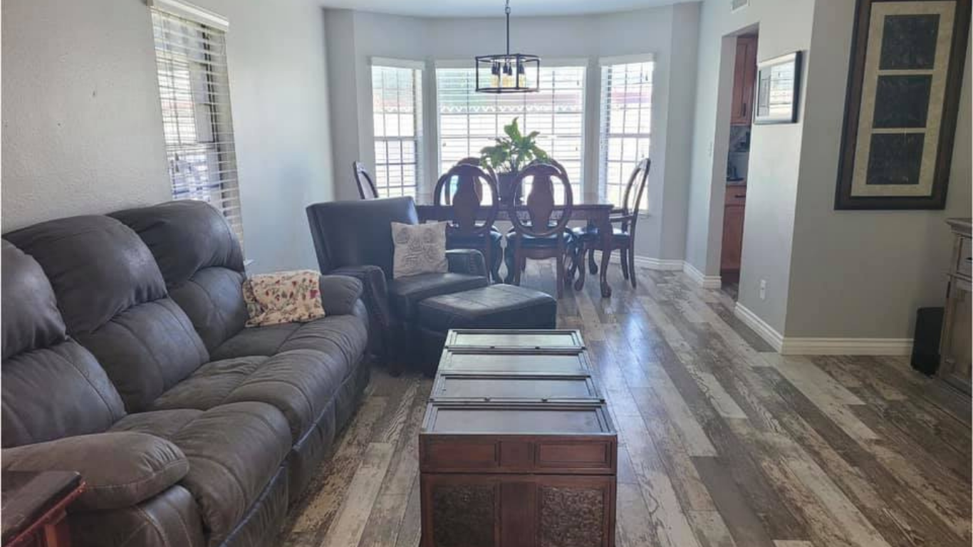 A gray living room with a large sofa, a dark chest coffee table, and a dining table set in a windowed alcove.
