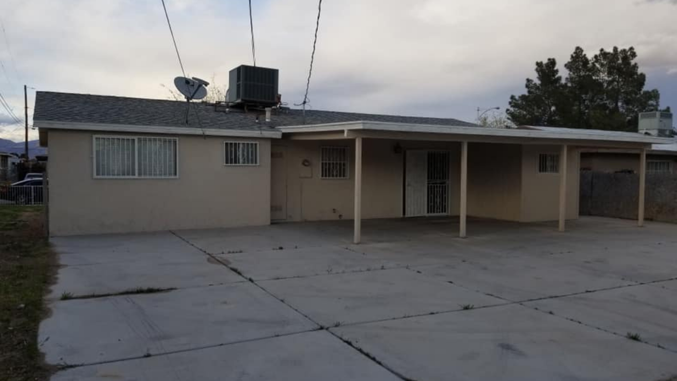 A single-story, beige house with a concrete driveway and a large covered patio extending from the side.