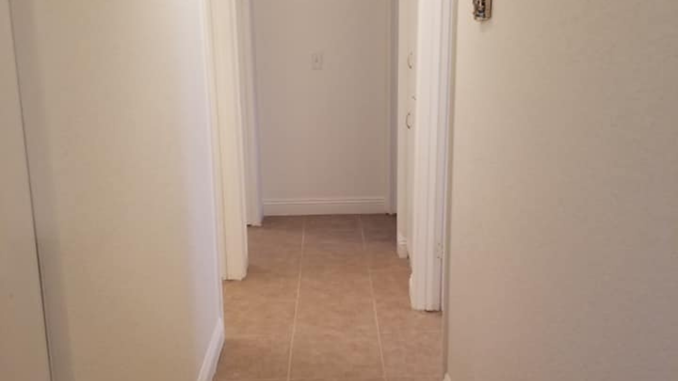 A brightly lit hallway with white walls, beige tile floors, and two doorways on the left and right sides.