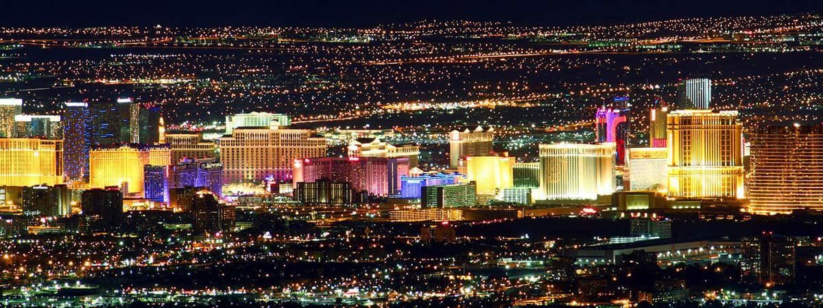 A panoramic night view of the illuminated Las Vegas Strip, featuring glowing hotels and skyscrapers under a dark sky.