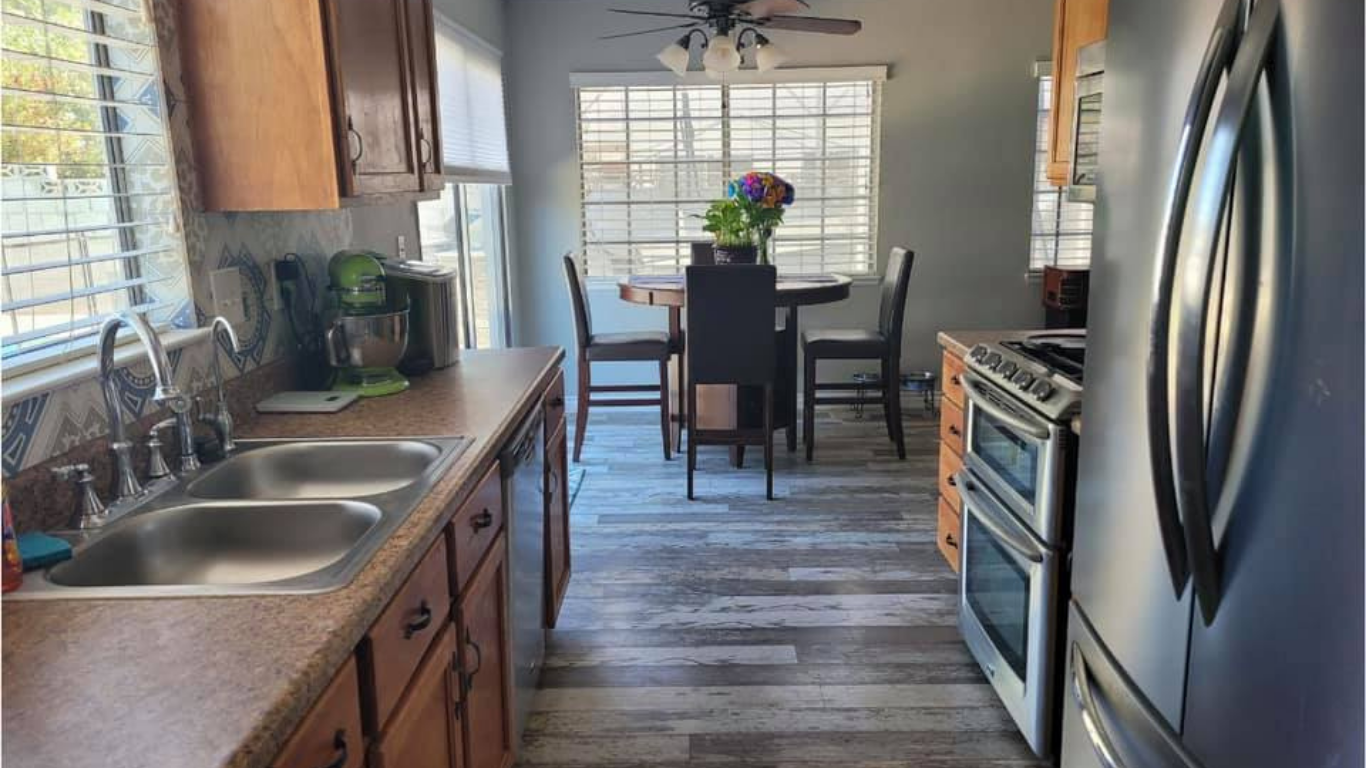 A kitchen with wooden cabinets, stainless steel appliances, a double sink, and a dining area with a table and chairs.