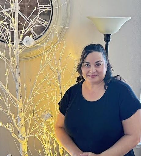 A woman in a black shirt is standing in front of a clock and a lamp.