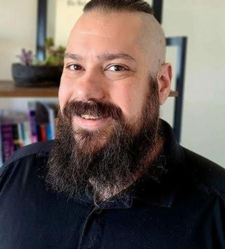 A man with a beard and mustache is wearing a black shirt and smiling.