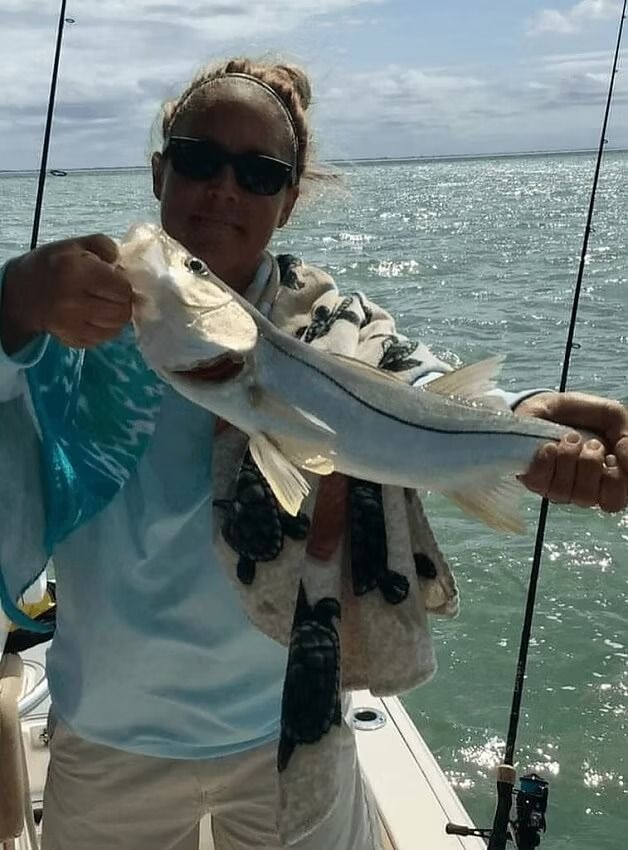 Woman on a boat holding a silver and white fish.  She's smiling, blue sky and water in the background.