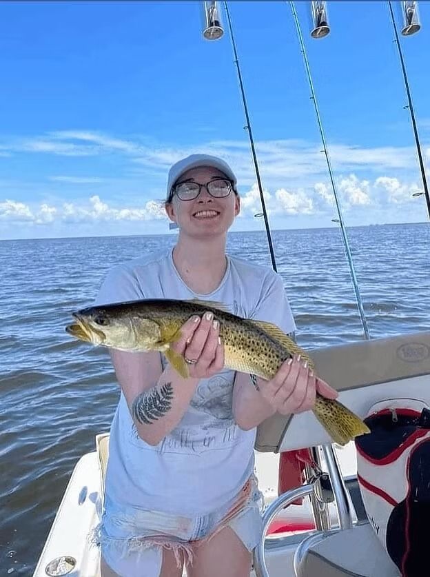 Woman on a boat smiles while holding a speckled trout she just caught.