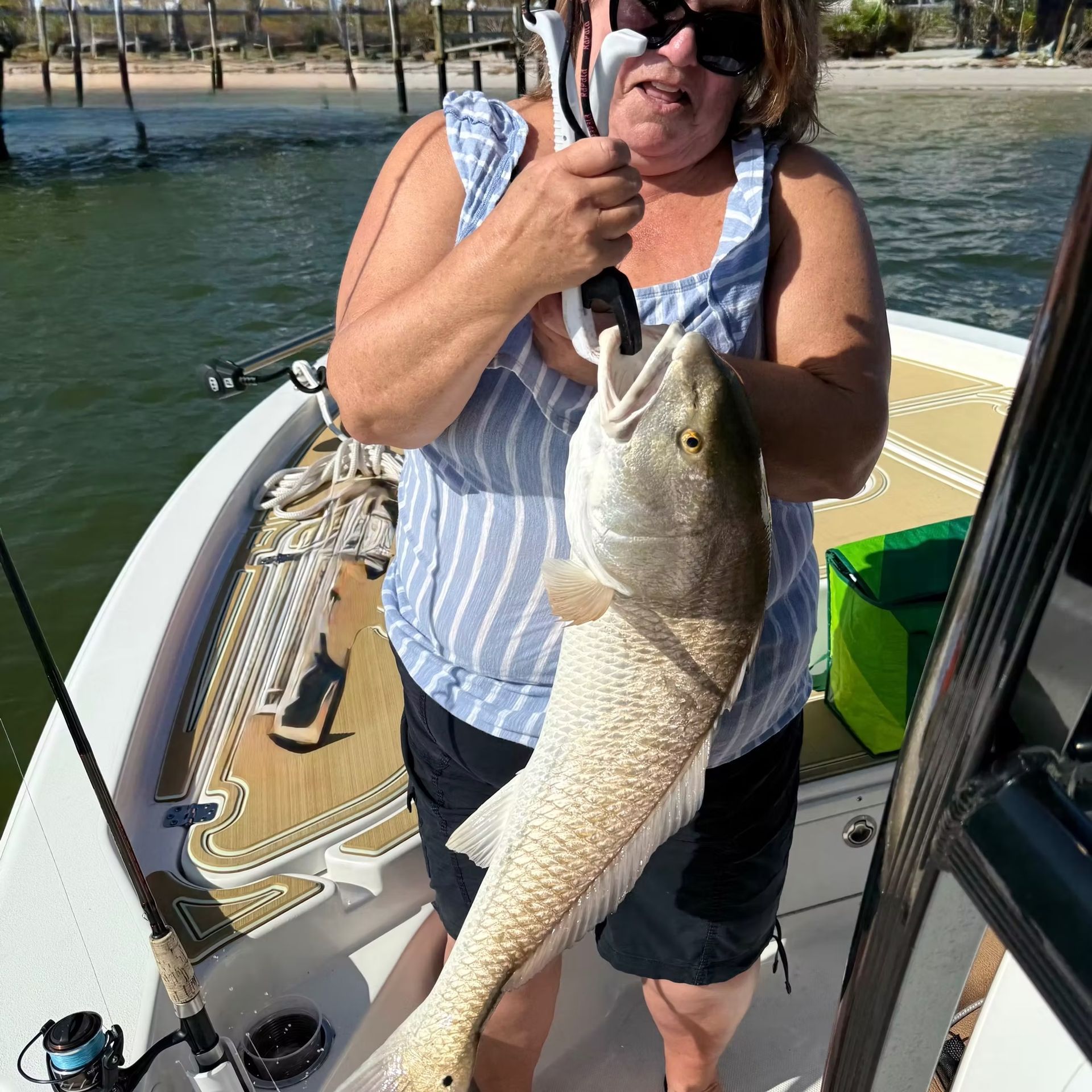 Woman on a boat holds up a large redfish caught fishing.