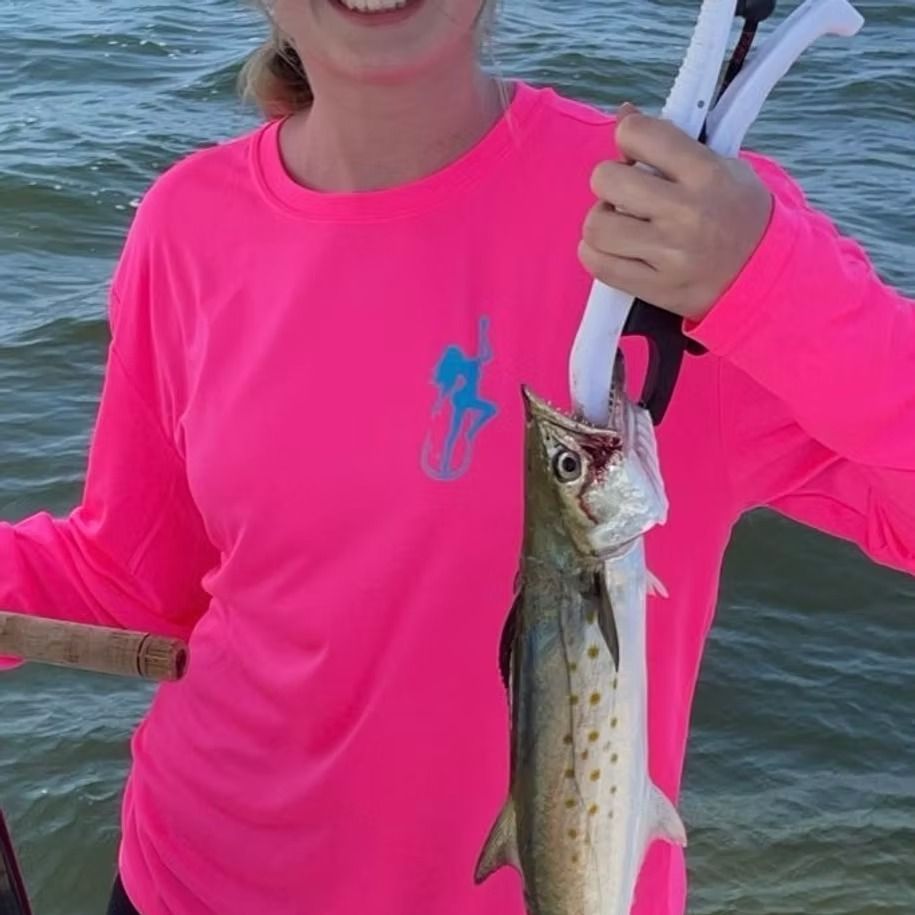 Woman in pink shirt holding a fish caught with fishing pliers. Ocean in the background.
