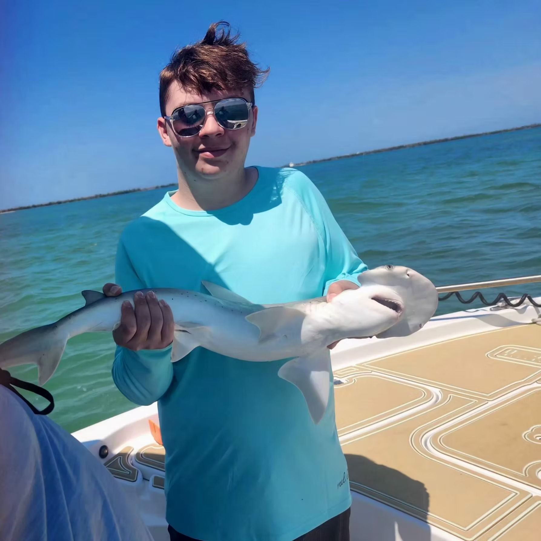 Young man in sunglasses holds a small hammerhead shark on a boat, sunny day on the water.
