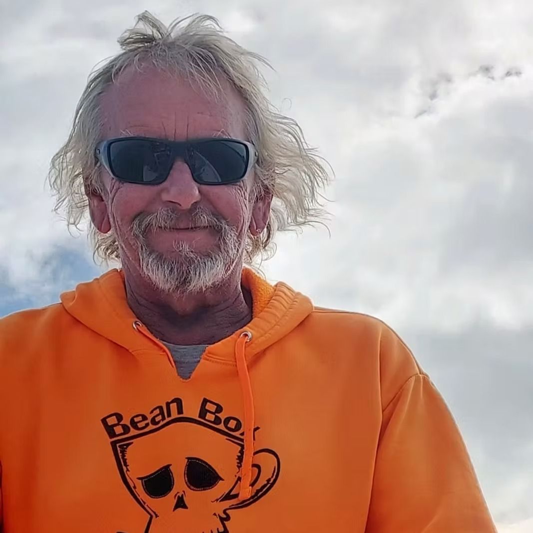 Man with gray hair, sunglasses, and orange hoodie. The hoodie reads 