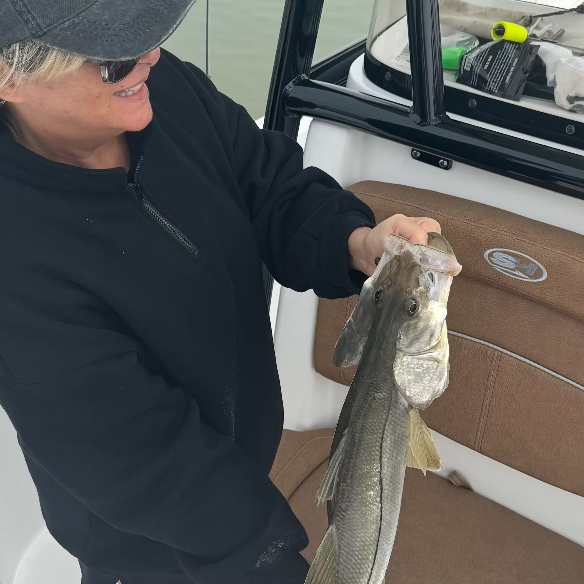 Woman on boat holds up a fish she caught, smiling.
