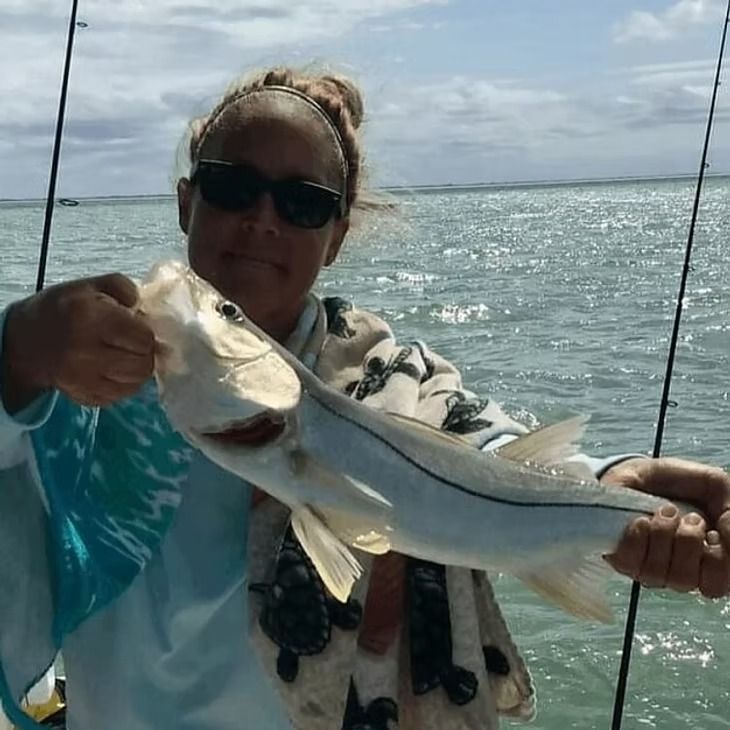 Woman holding a silver snook fish on a boat in the ocean, smiling, wearing sunglasses.