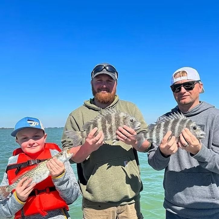 Three people on a boat fishing, holding up their catch in a bright blue sky.