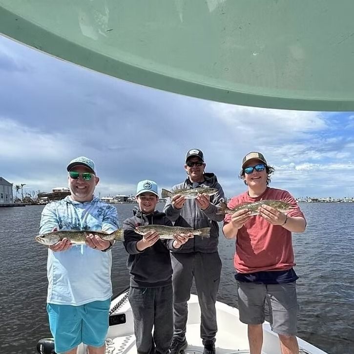 Four people on a boat hold up fish they caught. Cloudy day on the water.