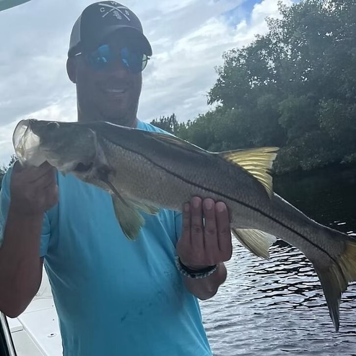 Man in blue shirt holding a silver snook fish on a boat.