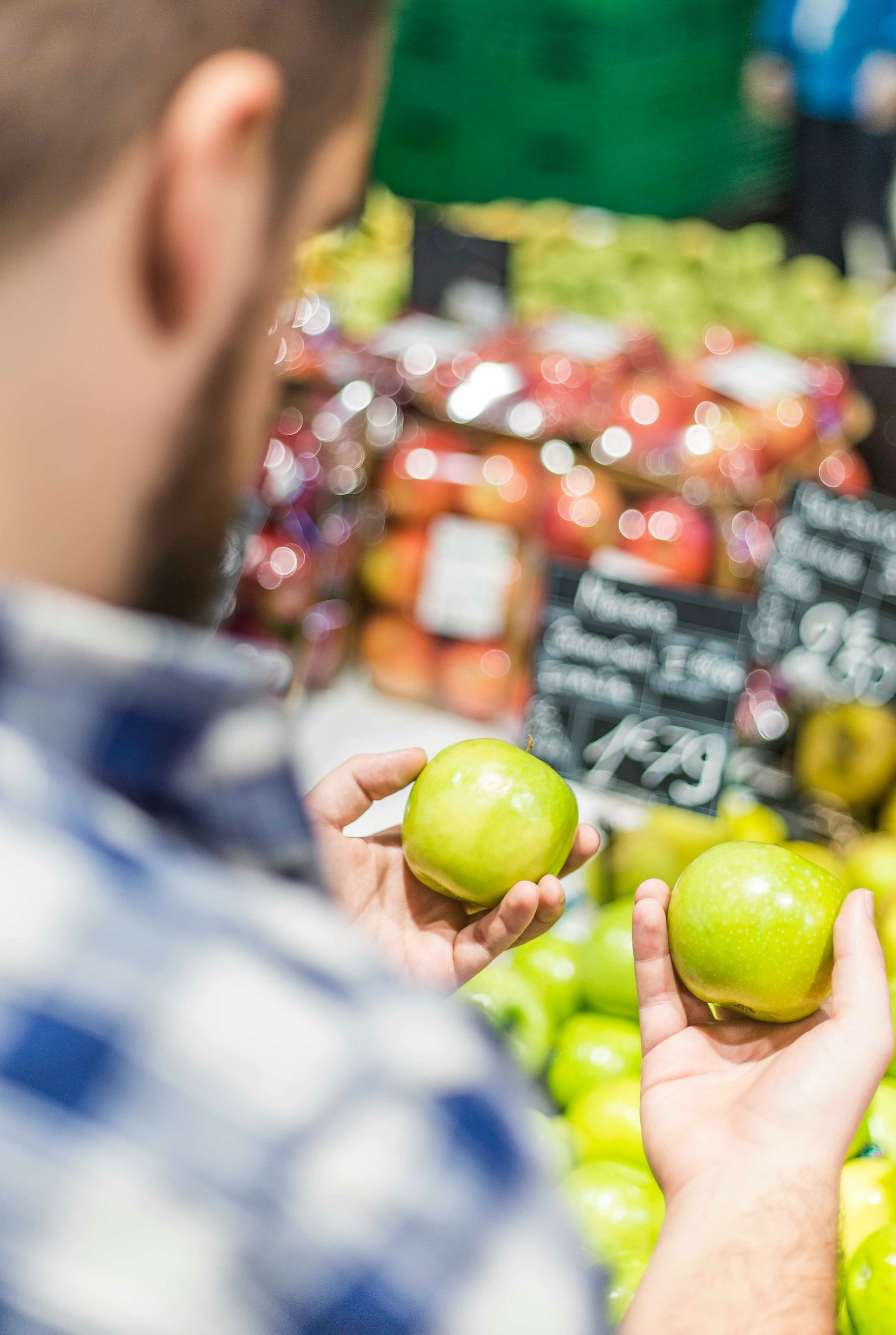 Een man inspecteert groene appels in de groenteafdeling van een supermarkt.