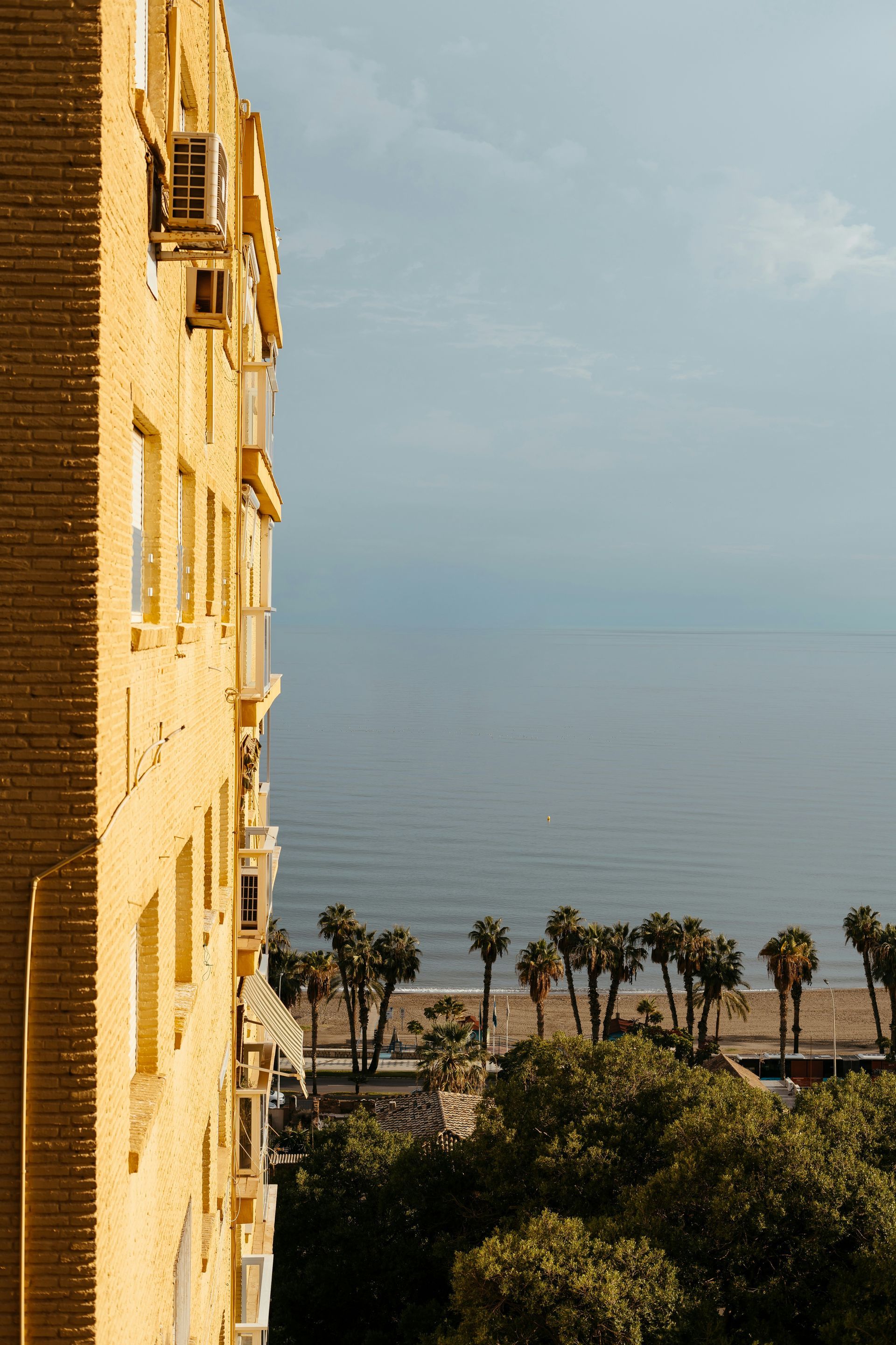 Geel gebouw, uitzicht op de oceaan. Palmbomen langs het strand. Bewolkte lucht.