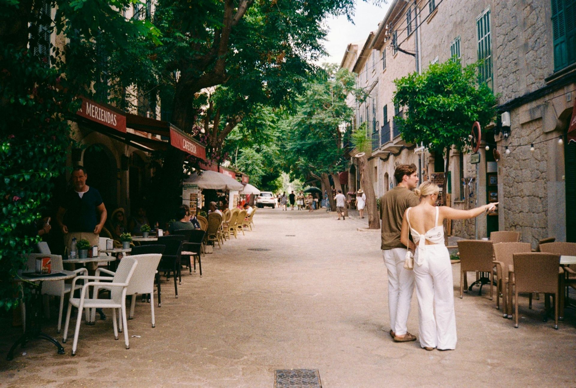 Een man en een vrouw lopen door een smalle straat met tafels en stoelen
