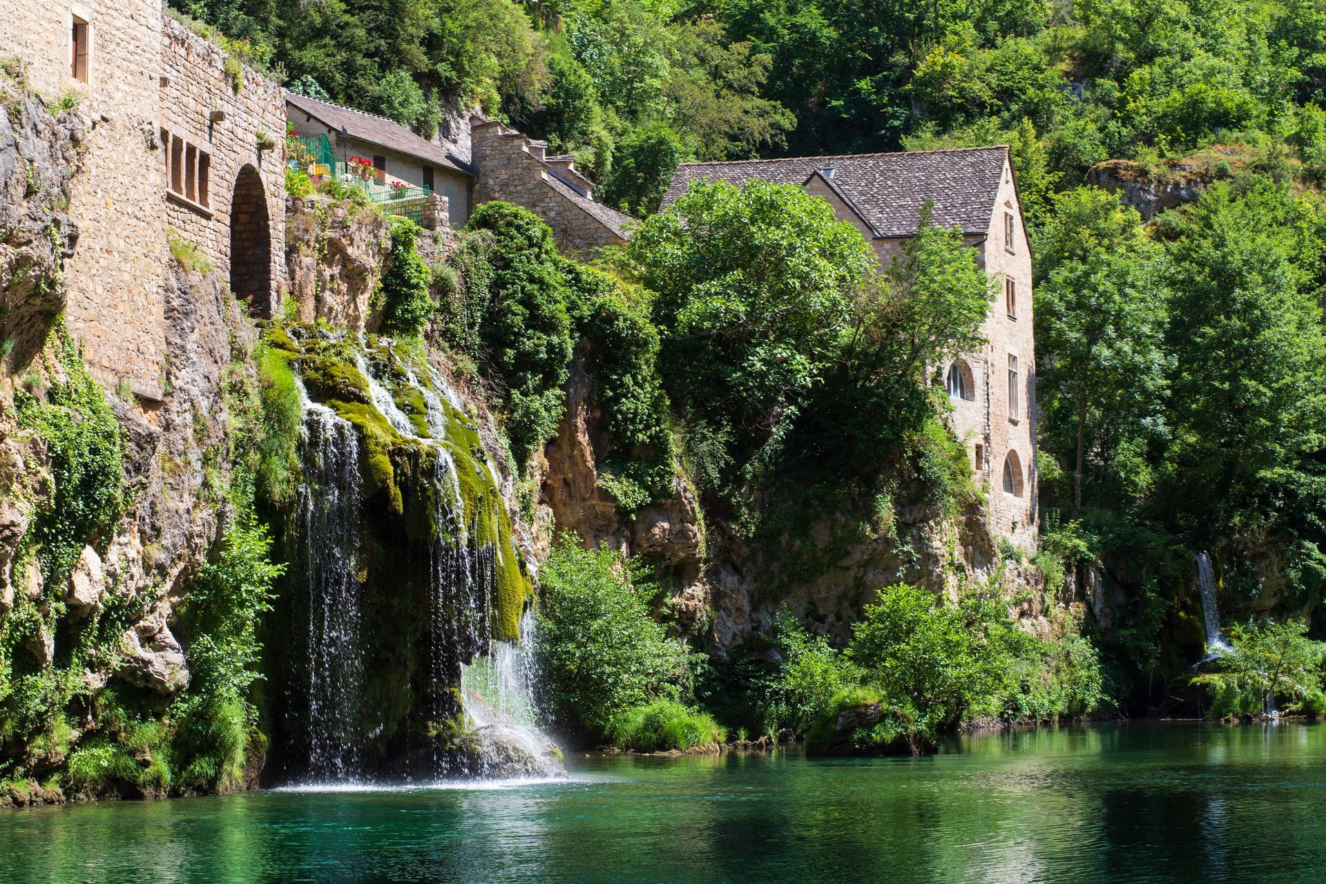 there is a waterfall in the middle of a lake with a building in the background .