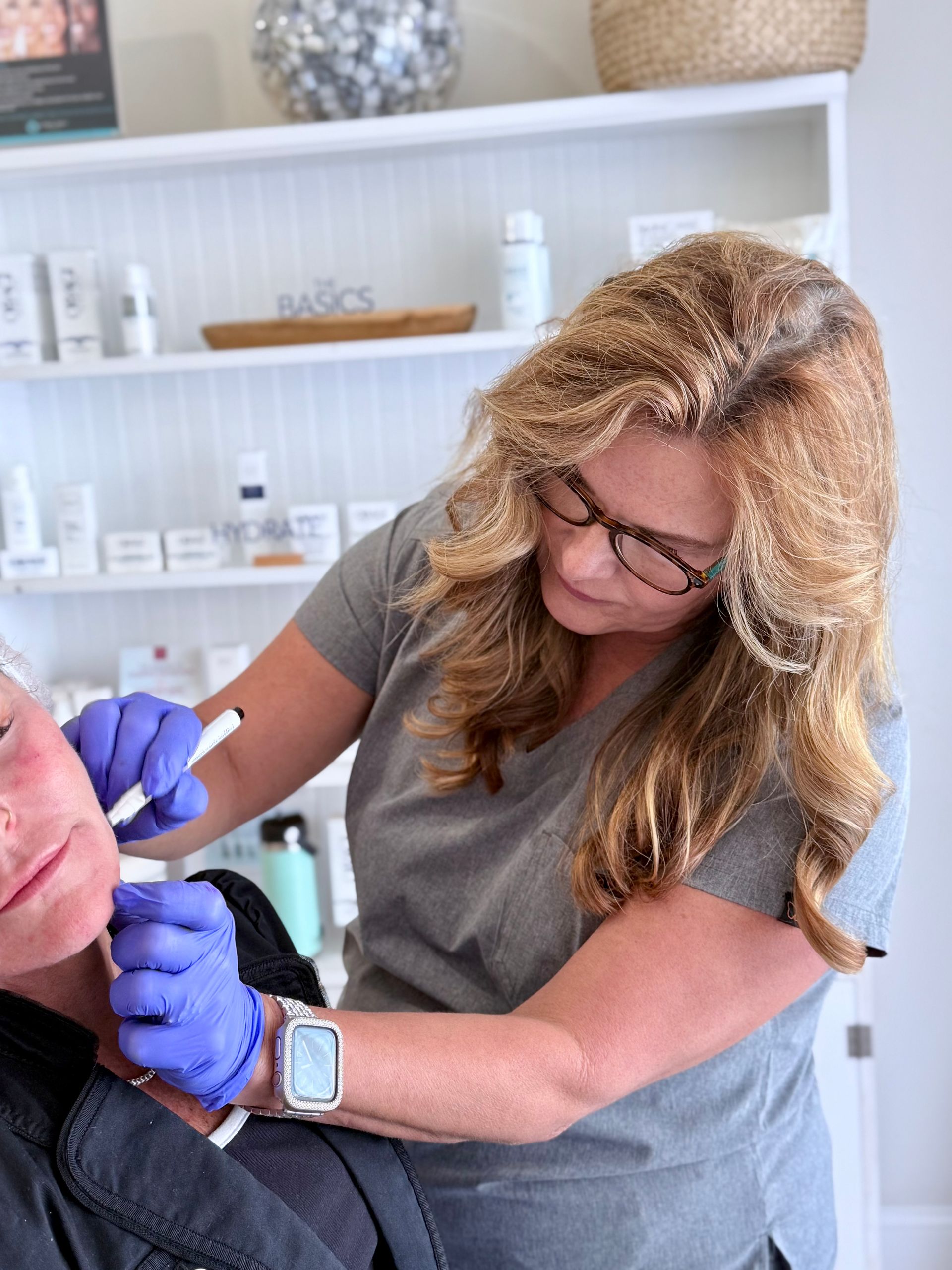 Woman receiving dermal filler injection to her jaw, being held by gloved hands.