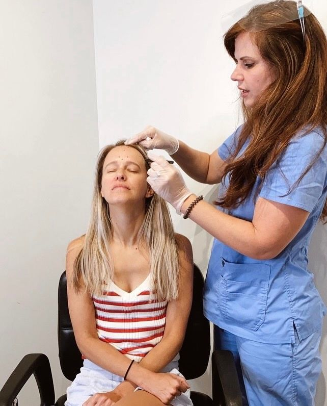 Woman looking up, fingers on temples, with a concerned expression against a blue-gray background.