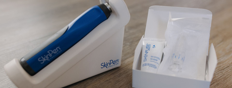 A blue SkinPen microneedling device on a white stand next to a box containing a small tube and sterile needle cartridges.