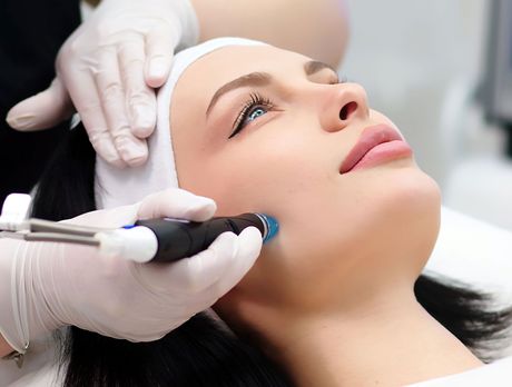 A professional receiving a facial treatment with a handheld device, with gloved hands applying it to their cheek.