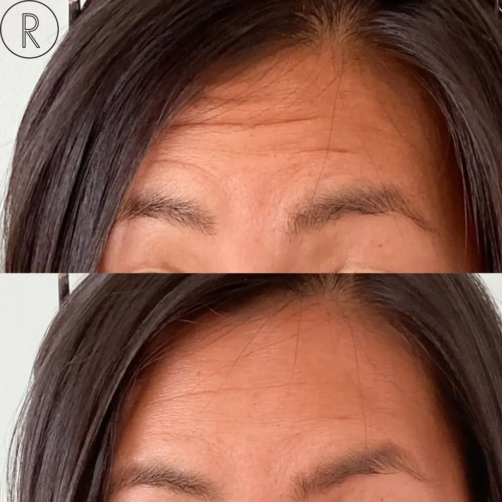 Woman with gray hair smiles, touching her face near the eyes in a bathroom.