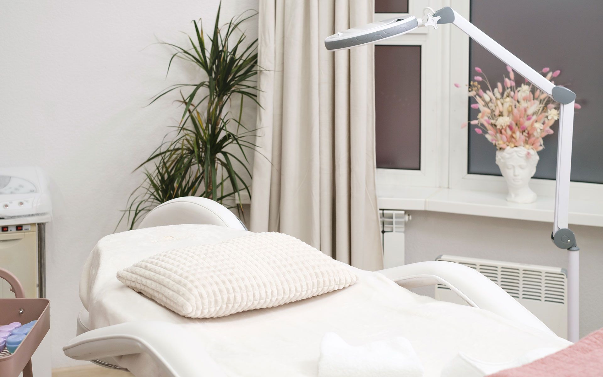 Treatment room with massage table, lamp, and window with flowers.