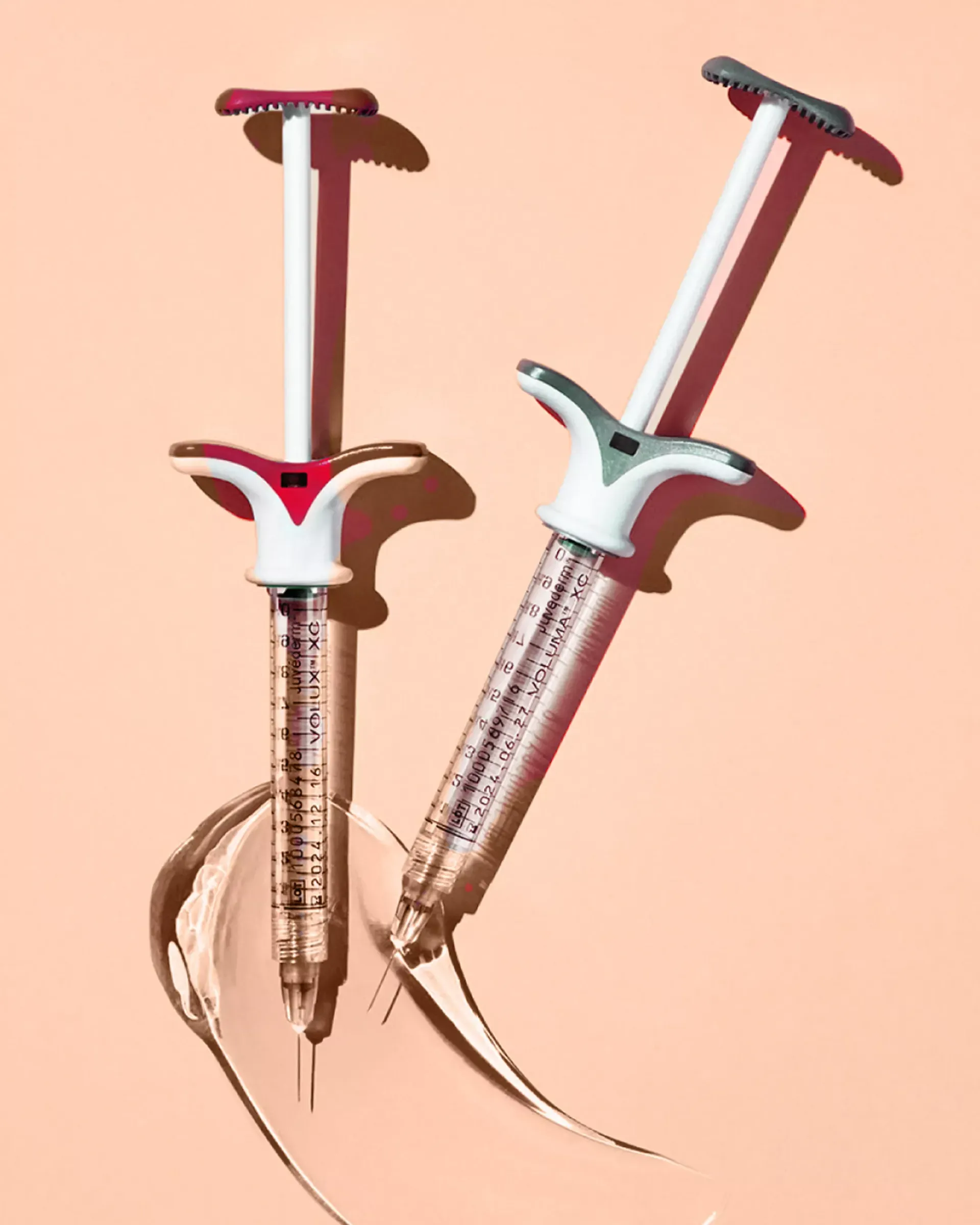 Two syringes with colored plungers, angled on a peach surface, with liquid spilling from the tips.