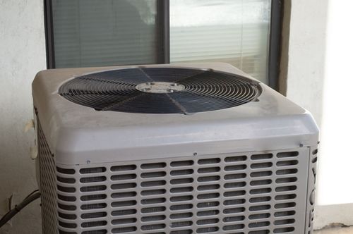 Outdoor air conditioner unit beside a window, with a black fan on top and vented front grille