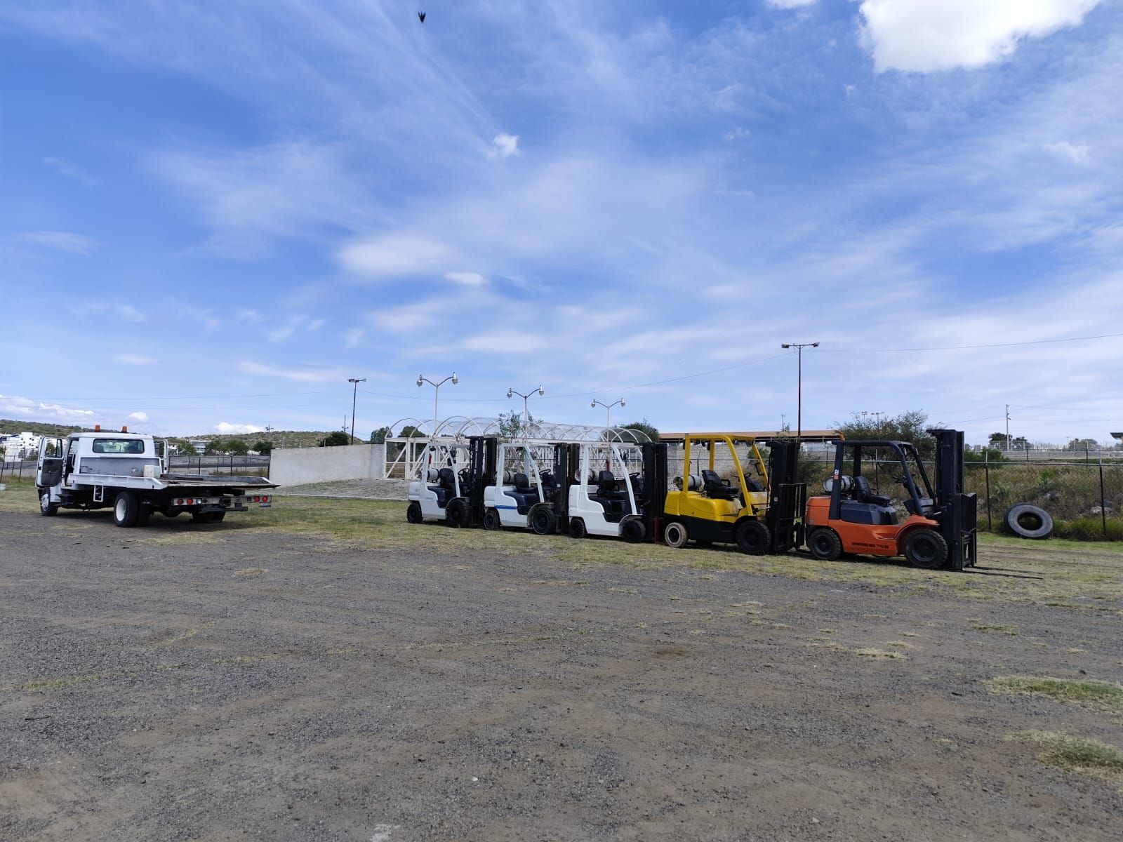 Una fila de carretillas elevadoras están estacionadas en un estacionamiento de grava.