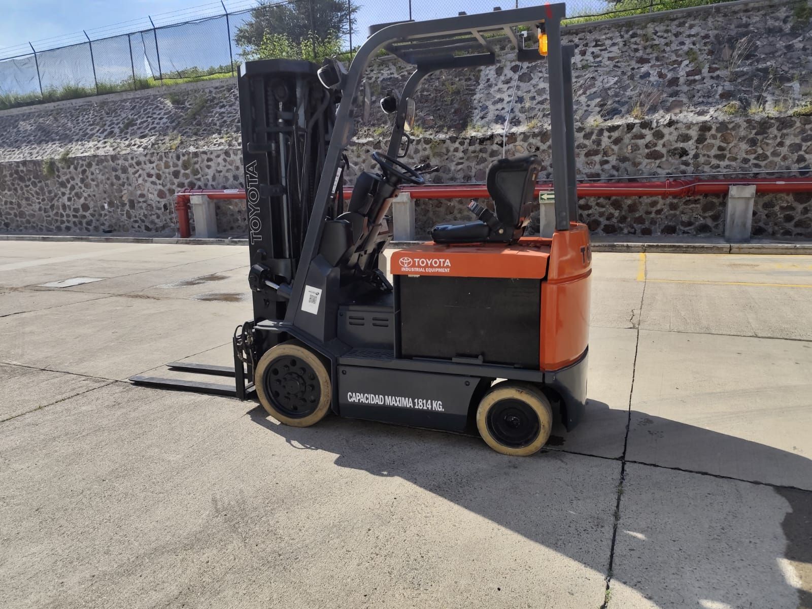 Una carretilla elevadora está estacionada en un estacionamiento frente a un muro de piedra.