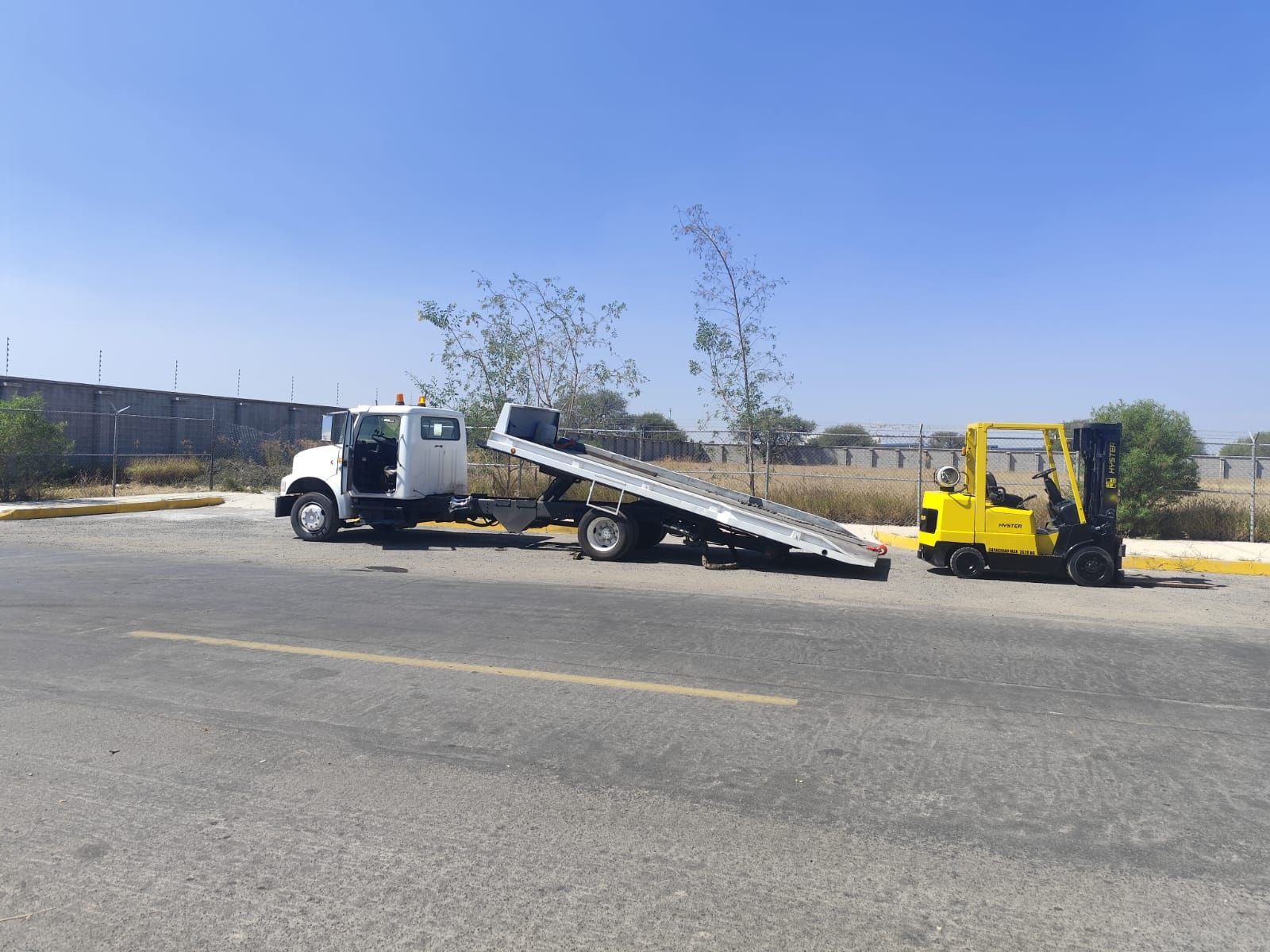 Una grúa blanca con una carretilla elevadora amarilla acoplada a ella.