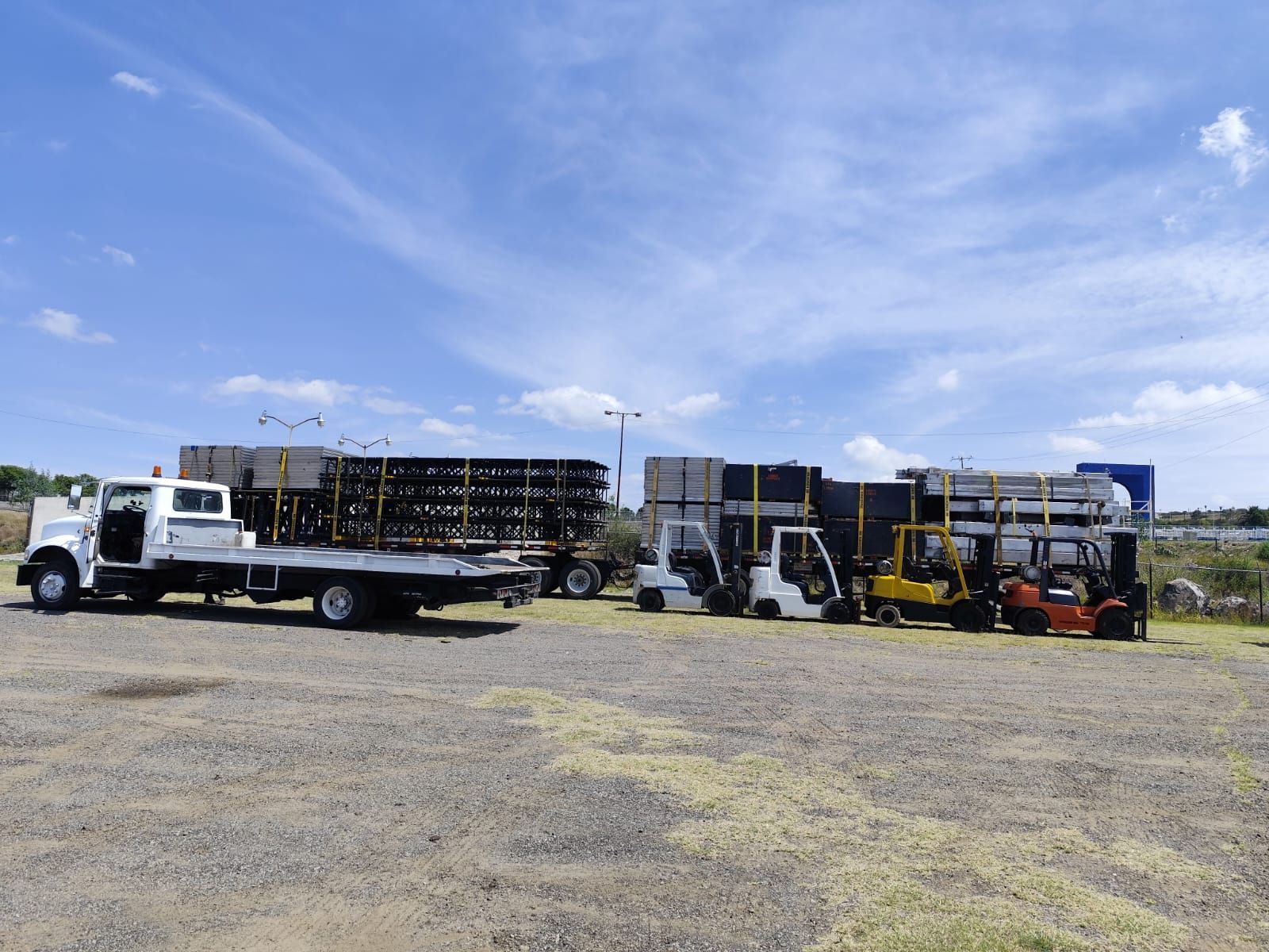 Un camión de plataforma está estacionado al lado de una carretilla elevadora en un estacionamiento de grava.