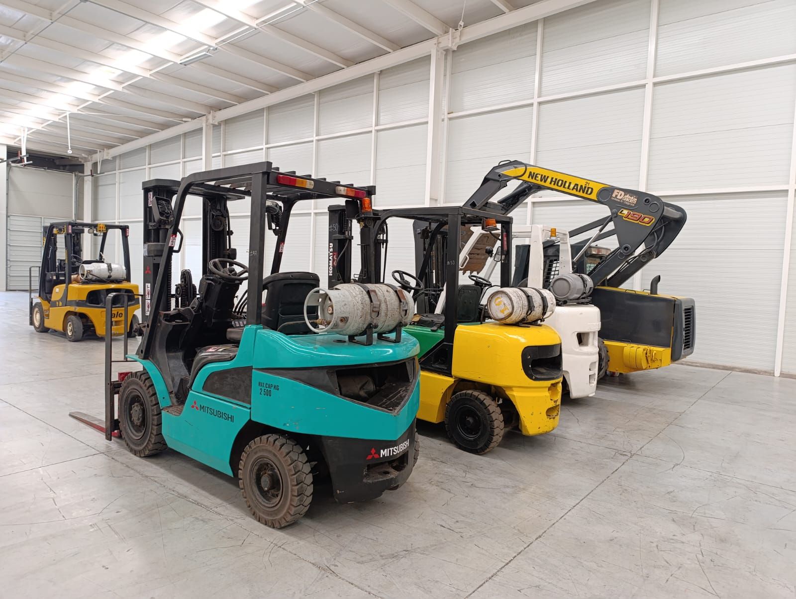 Una fila de carretillas elevadoras están estacionadas en un almacén.